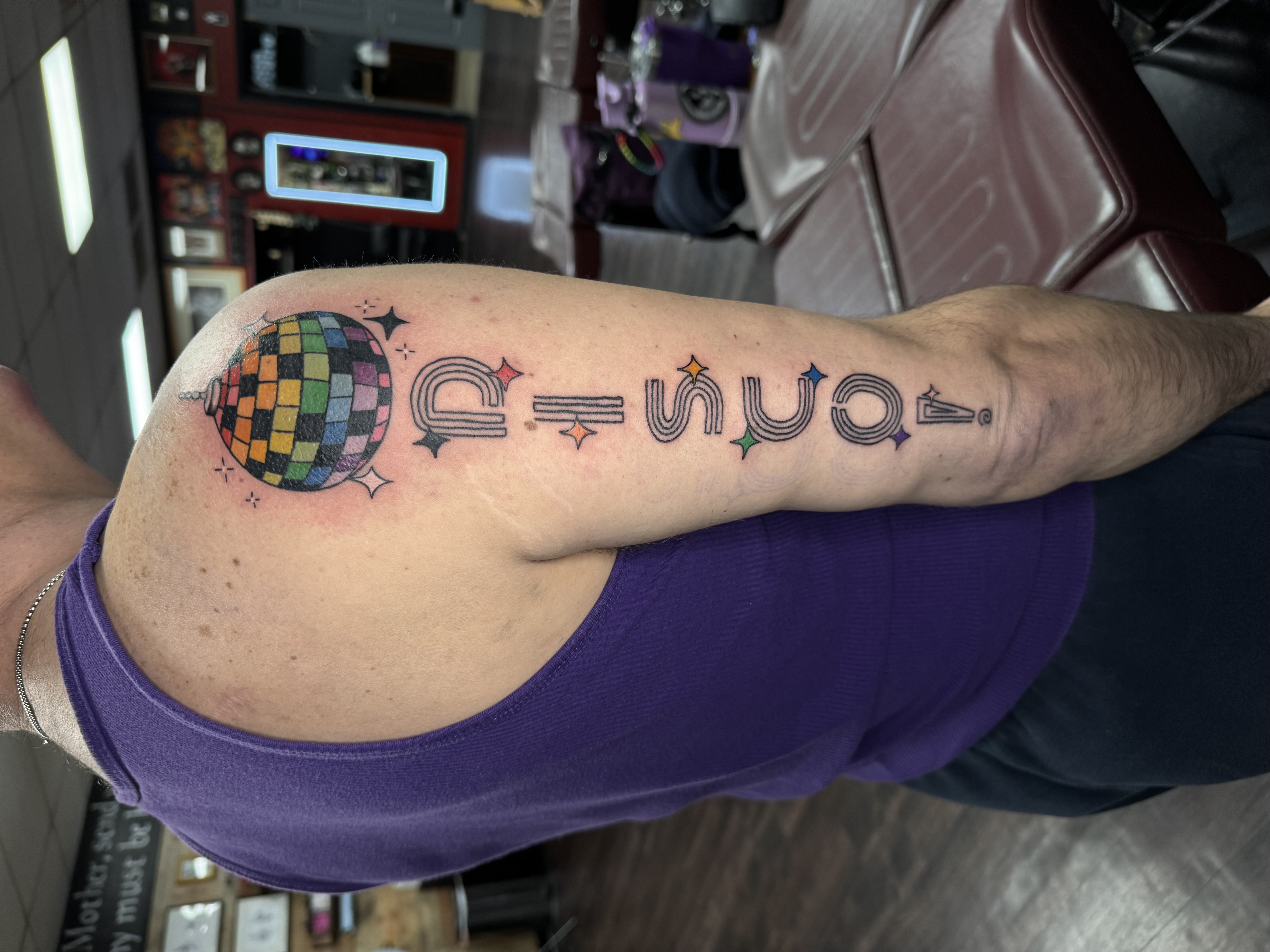 photo of finished tattoo of rainbow disco ball on right shoulder with DISCO! vertically down the tricep below it and ending at the right elbow